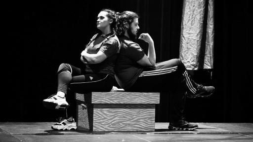 Actors on stage sitting back to back